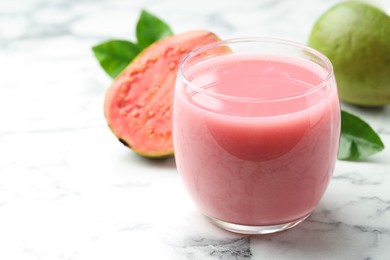 Photo of Tasty guava juice in glass, leaves and fruits on white marble table, closeup. Space for text