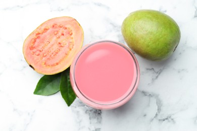 Photo of Tasty guava juice in glass, leaves and fruits on white marble table, flat lay