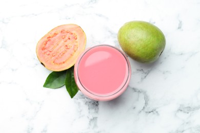 Photo of Tasty guava juice in glass, leaves and fruits on white marble table, flat lay