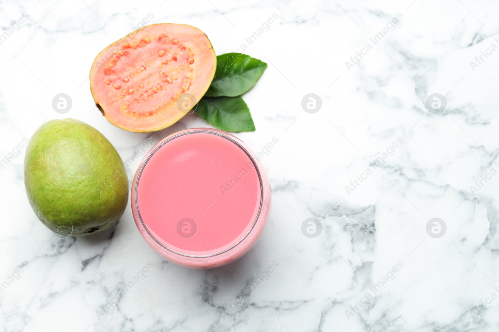 Photo of Tasty guava juice in glass, leaves and fruits on white marble table, flat lay. Space for text