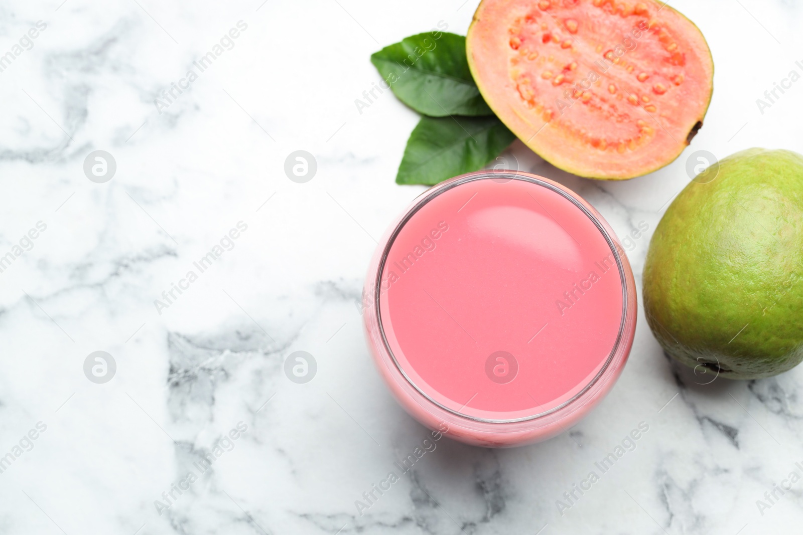 Photo of Tasty guava juice in glass, leaves and fruits on white marble table, flat lay. Space for text