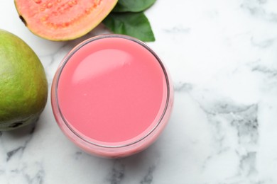 Photo of Tasty guava juice in glass, leaves and fruits on white marble table, flat lay. Space for text