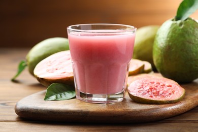 Photo of Tasty guava juice in glass, leaves and fruits on wooden table, closeup