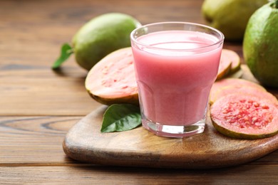 Photo of Tasty guava juice in glass, leaves and fruits on wooden table, closeup