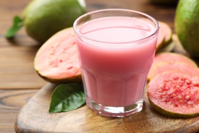 Photo of Tasty guava juice in glass, leaves and fruits on wooden table, closeup