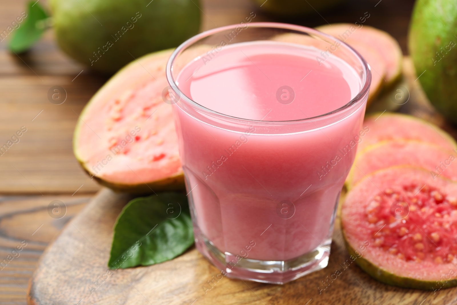 Photo of Tasty guava juice in glass, leaf and fruits on wooden table, closeup