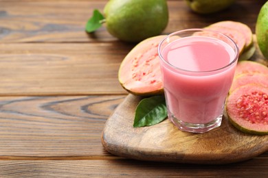 Photo of Tasty guava juice in glass, leaf and fruits on wooden table, closeup. Space for text