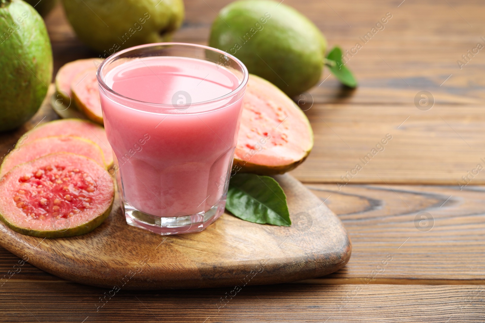 Photo of Tasty guava juice in glass, leaf and fruits on wooden table, closeup. Space for text