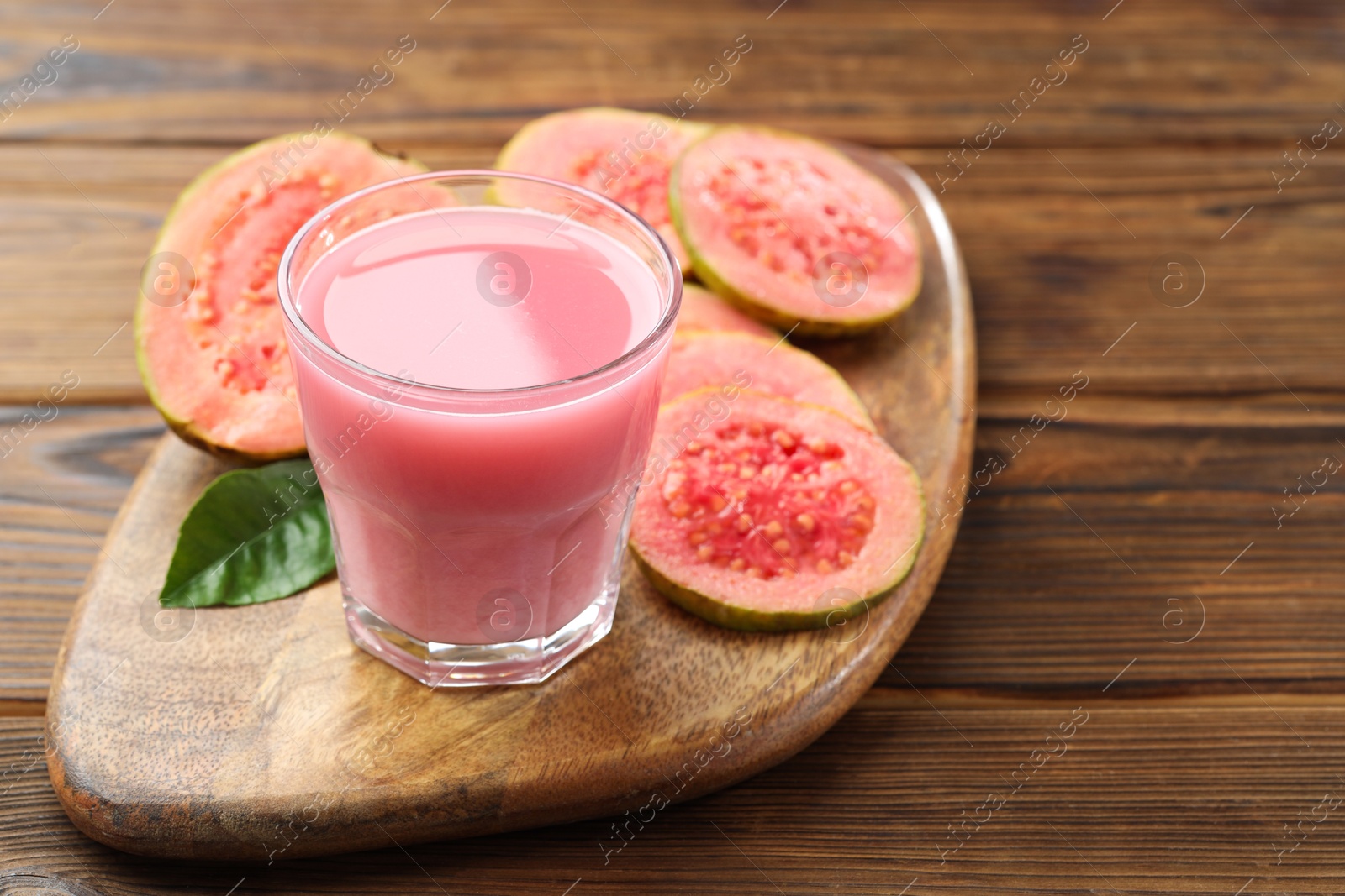 Photo of Tasty guava juice in glass, leaf and slices of fruits on wooden table, closeup