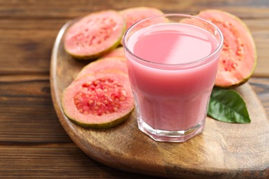 Photo of Tasty guava juice in glass, leaf and slices of fruits on wooden table, closeup