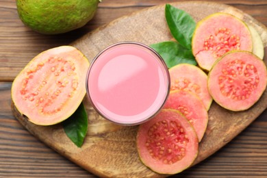 Photo of Tasty guava juice in glass, leaves and slices of fruits on wooden table, flat lay