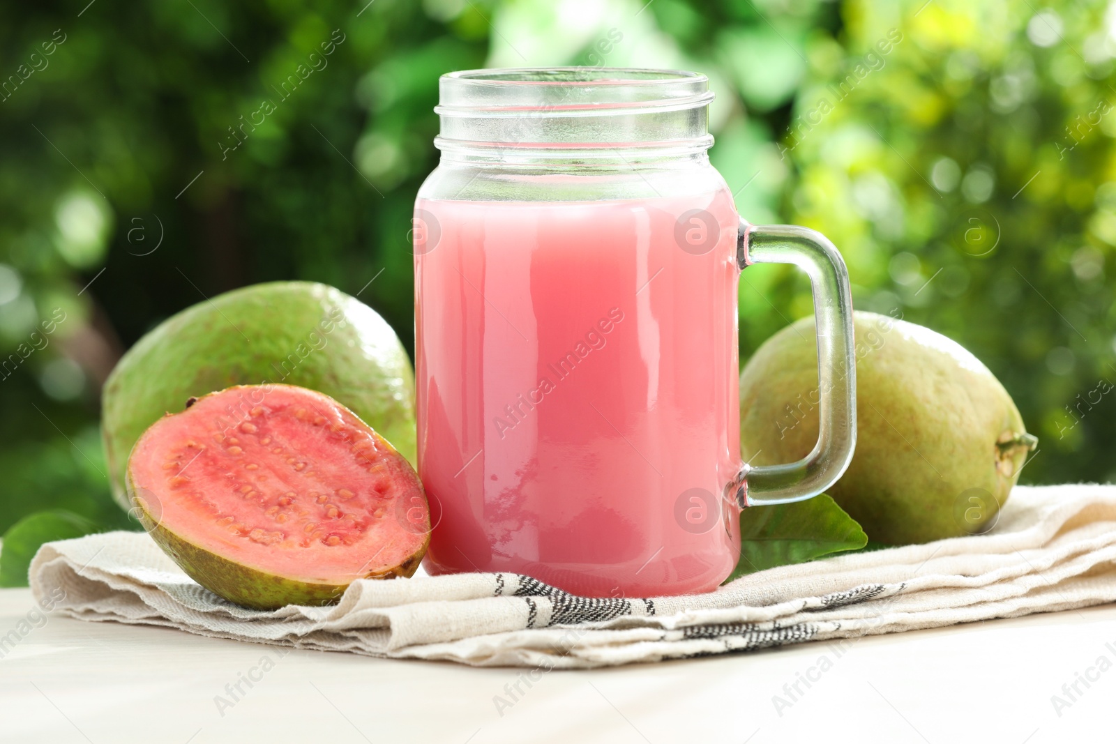 Photo of Tasty guava juice in mason jar and fresh fruits on white table outdoors, closeup