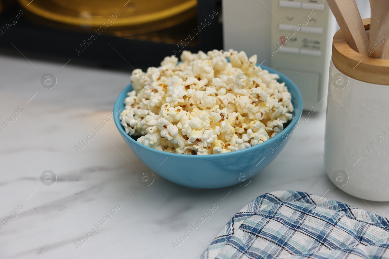 Photo of Tasty popcorn in bowl near microwave oven on white marble table, closeup