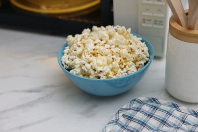 Photo of Tasty popcorn in bowl near microwave oven on white marble table, closeup