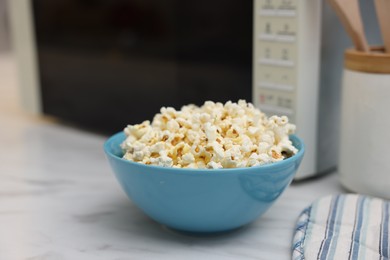 Photo of Tasty popcorn in bowl near microwave oven on white marble table, closeup. Space for text