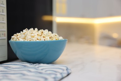 Photo of Tasty popcorn in bowl near microwave oven on white table indoors, space for text