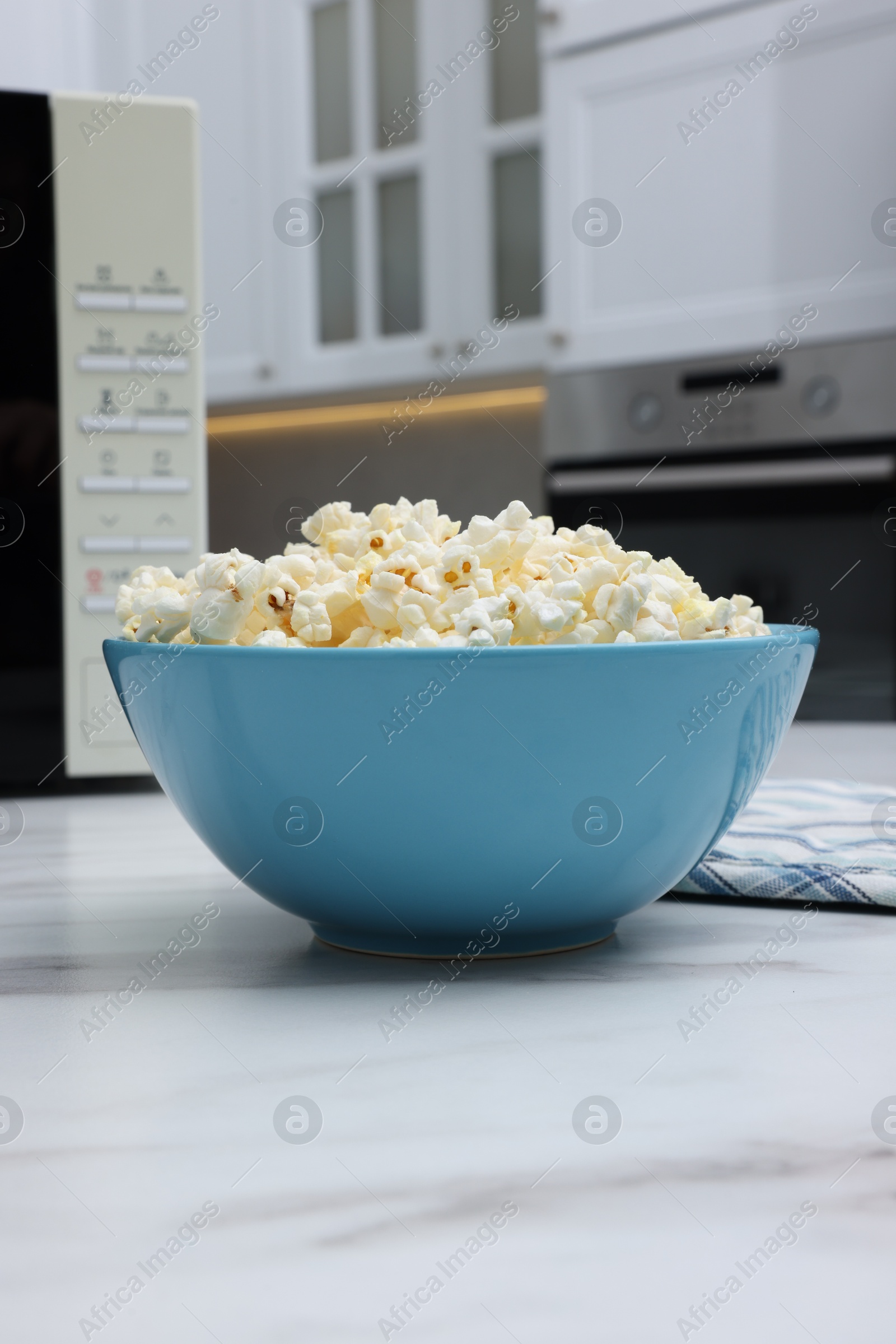 Photo of Tasty popcorn in bowl n on white marble table indoors