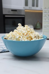 Photo of Tasty popcorn in bowl n on white marble table indoors