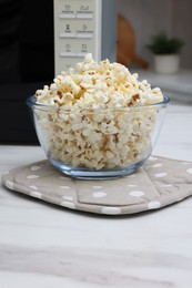 Photo of Tasty popcorn in bowl near microwave oven on white marble table indoors