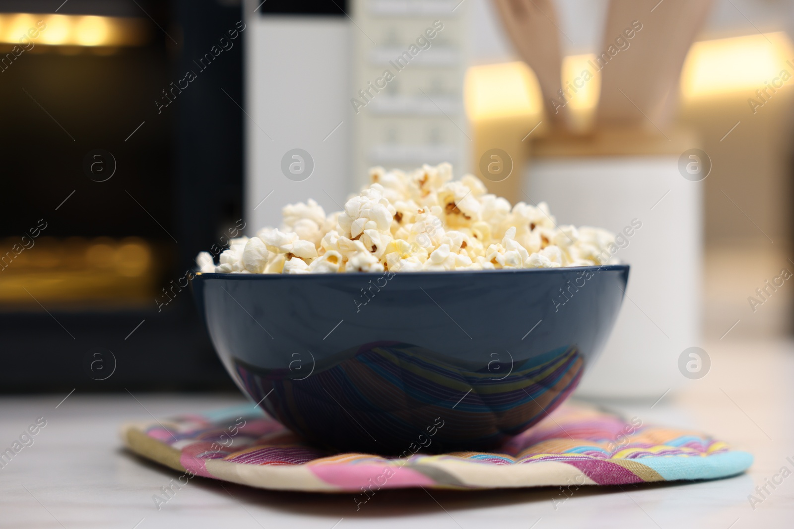 Photo of Tasty popcorn in bowl near microwave oven on light table indoors, closeup