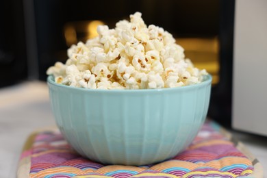 Photo of Tasty popcorn in bowl near microwave oven on table, closeup