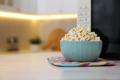 Photo of Tasty popcorn in bowl near microwave oven on light marble table indoors, space for text