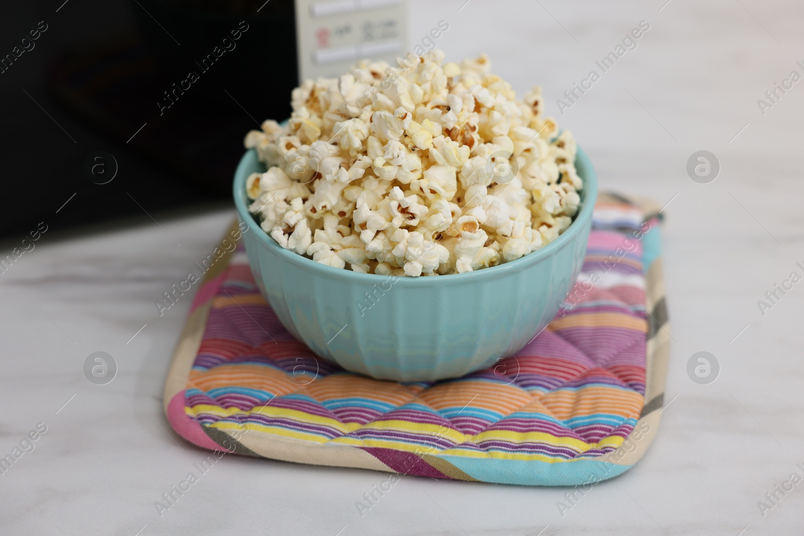 Photo of Tasty popcorn in bowl near microwave oven on light marble table, closeup