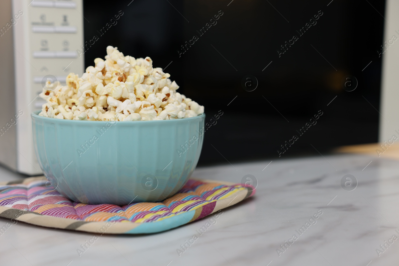 Photo of Tasty popcorn in bowl near microwave oven on light marble table, closeup. Space for text