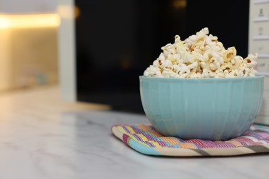 Photo of Tasty popcorn in bowl near microwave oven on light marble table, closeup. Space for text