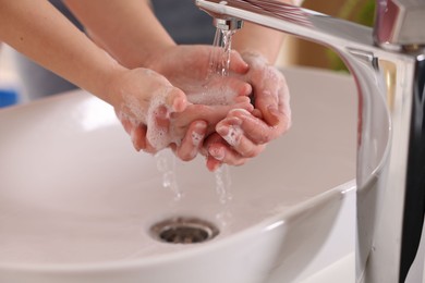 Photo of Mother and daughter washing their hands above sink indoors, closeup