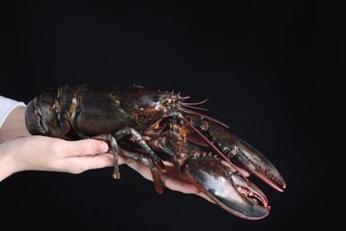 Photo of Woman with raw lobster on black background, closeup