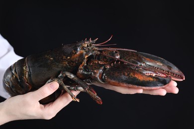 Photo of Woman with raw lobster on black background, closeup