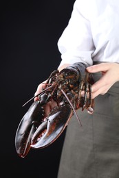 Photo of Woman with raw lobster on black background, closeup