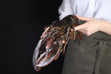 Photo of Woman with raw lobster on black background, closeup. Space for text