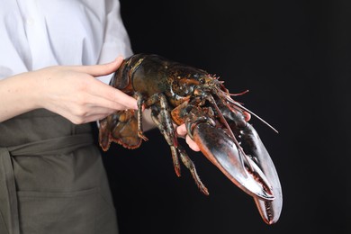 Photo of Woman with raw lobster on black background, closeup