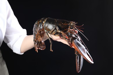 Photo of Woman with raw lobster on black background, closeup