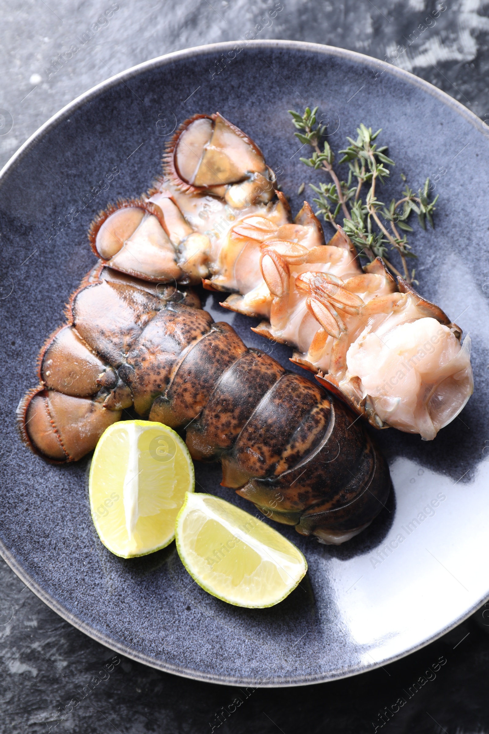 Photo of Raw lobster tails, lime and thyme on dark table, top view