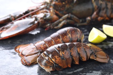 Photo of Raw lobster, tails and lime on dark table, closeup