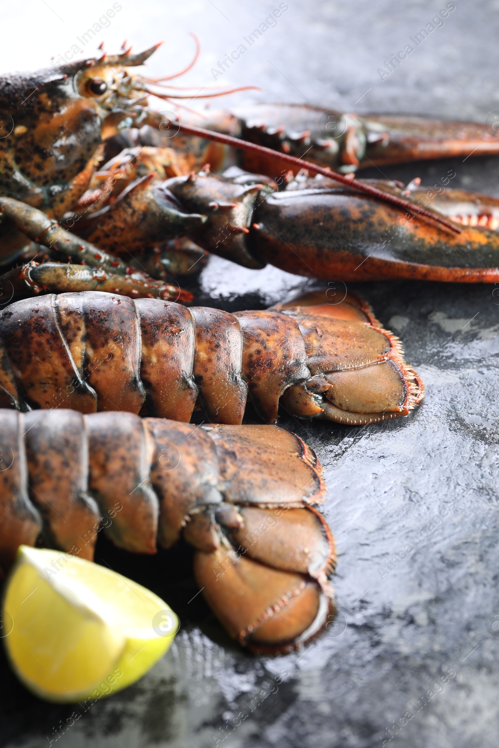 Photo of Raw lobster, tails and lime on dark table, closeup