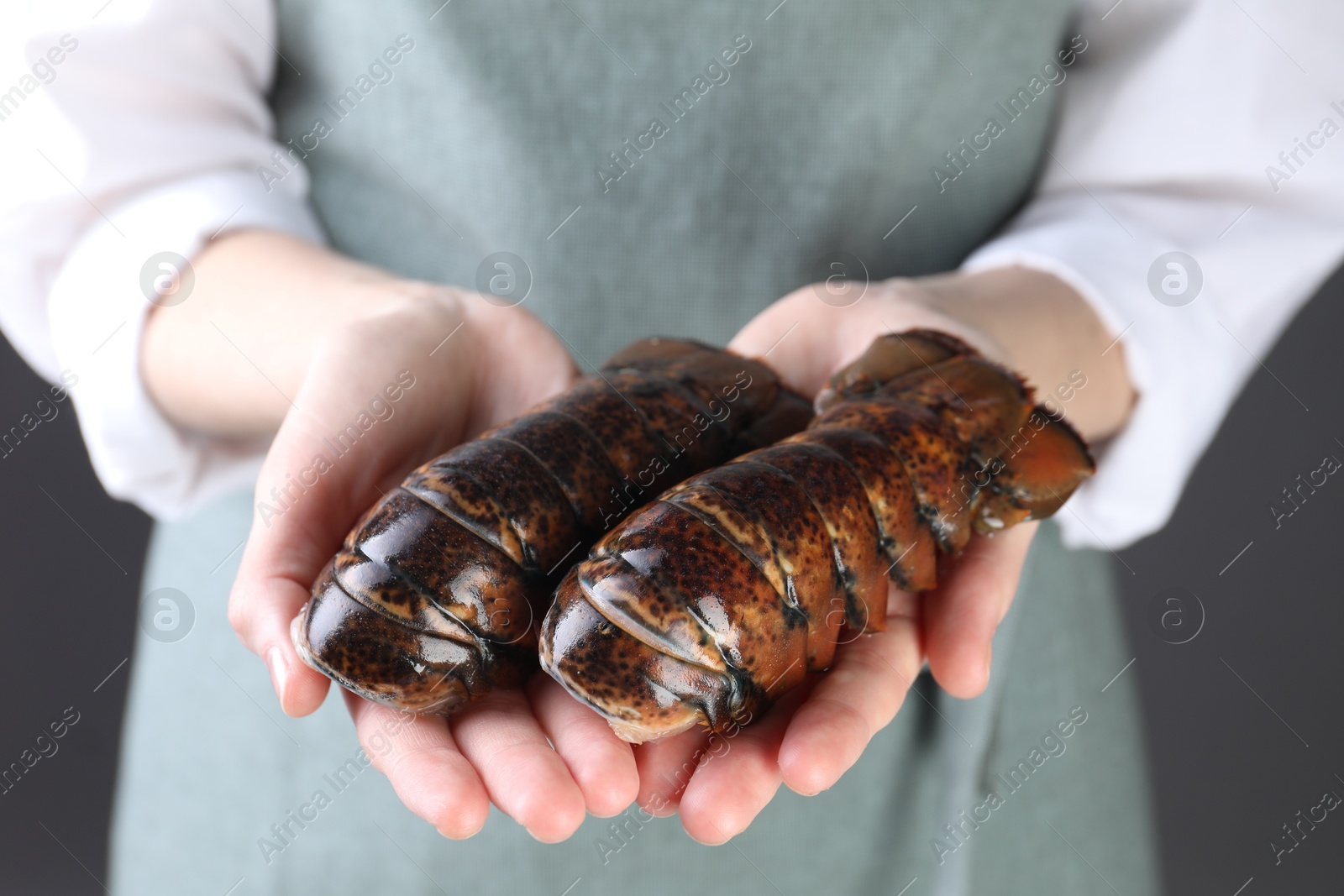 Photo of Woman with raw lobster tails on dark grey background, closeup