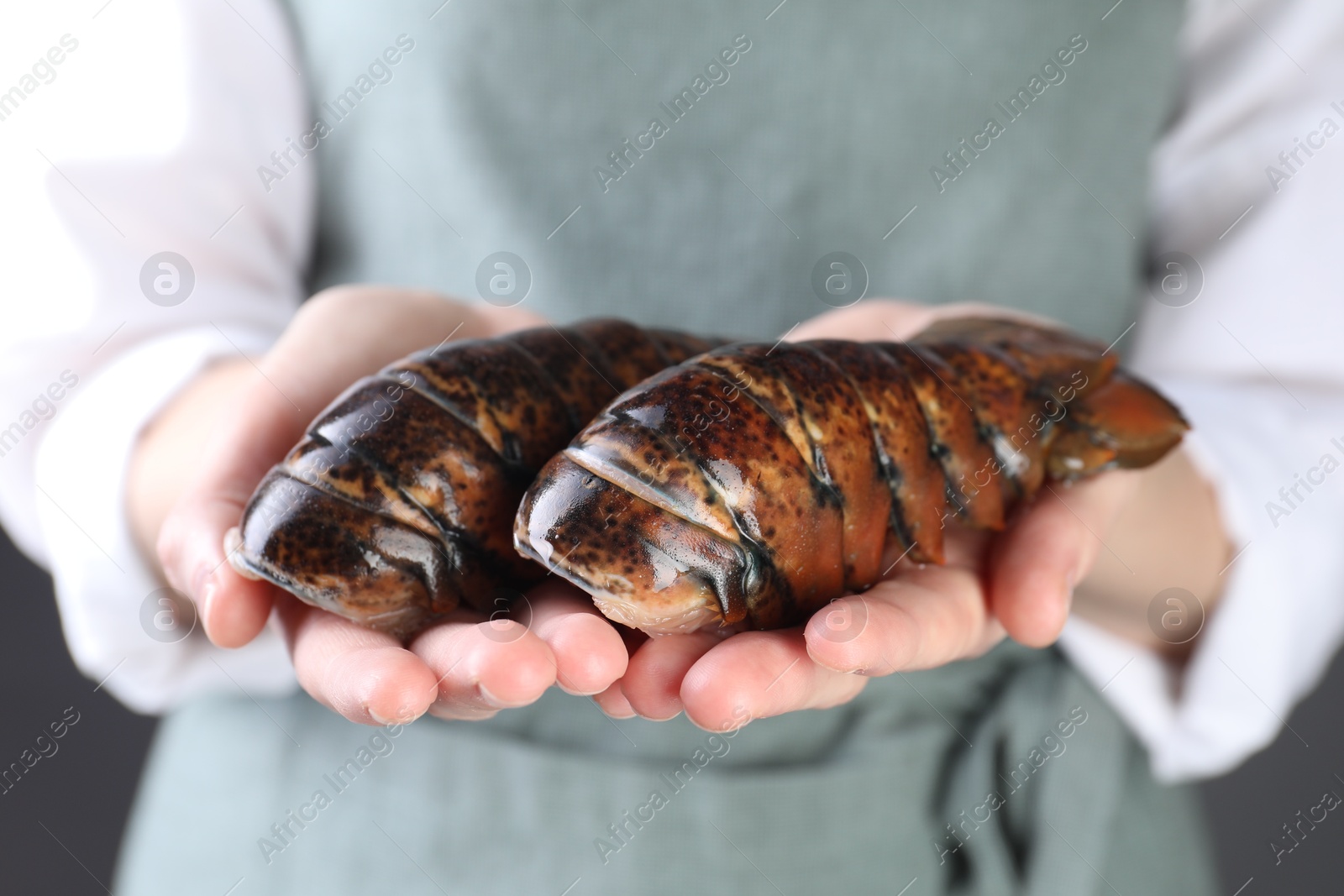 Photo of Woman with raw lobster tails on dark grey background, closeup