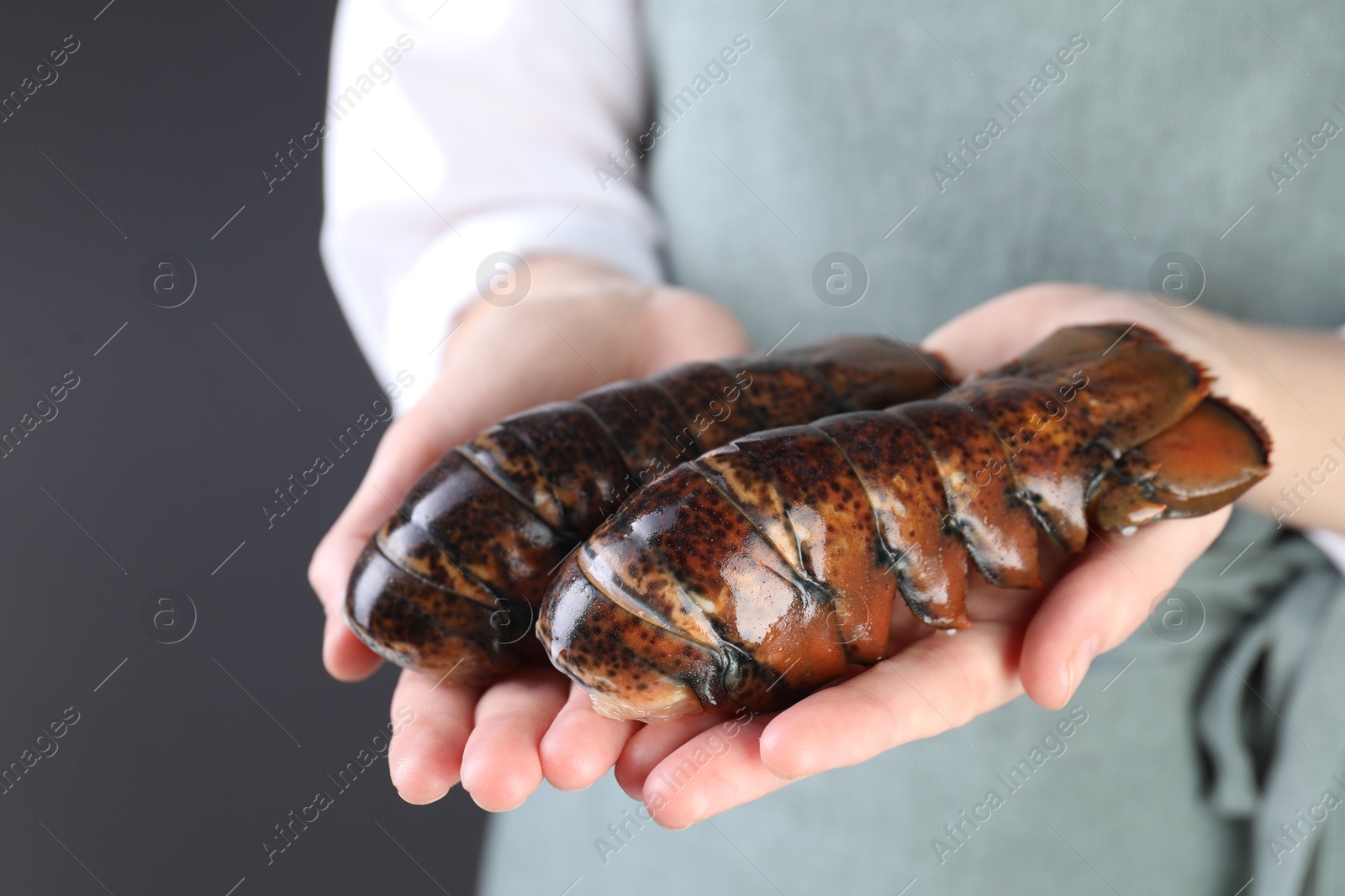 Photo of Woman with raw lobster tails on dark grey background, closeup