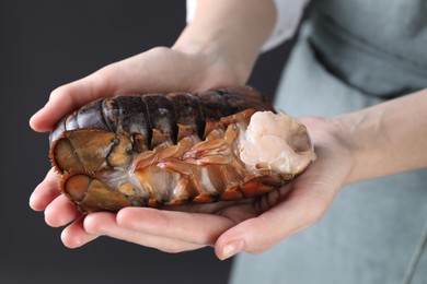 Photo of Woman with raw lobster tails on dark grey background, closeup