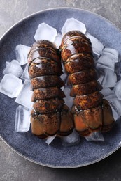 Photo of Raw lobster tails with ice on grey table, top view