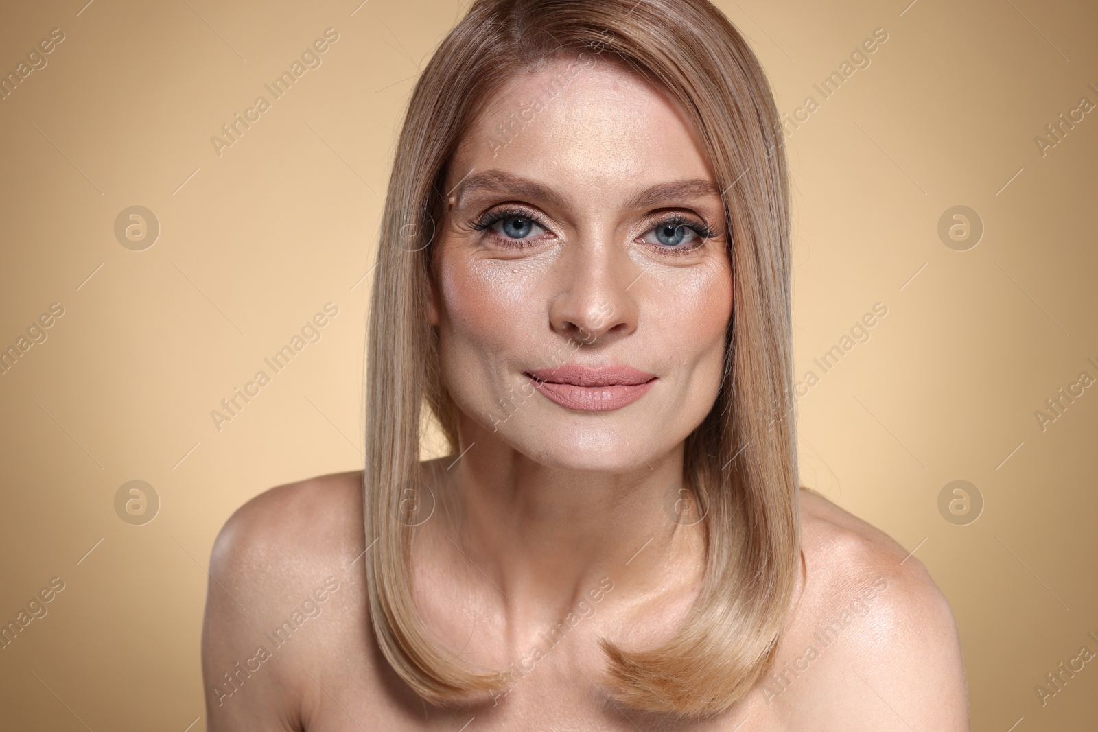 Photo of Beautiful woman with straight blonde hair and stylish makeup on beige background