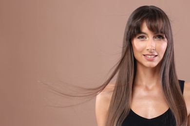 Photo of Hair styling. Portrait of beautiful woman with straight long hair on pale brown background