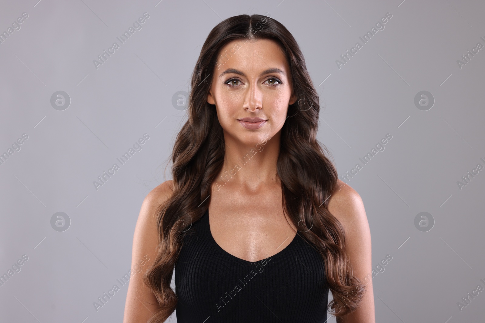 Photo of Hair styling. Portrait of beautiful woman with wavy long hair on grey background