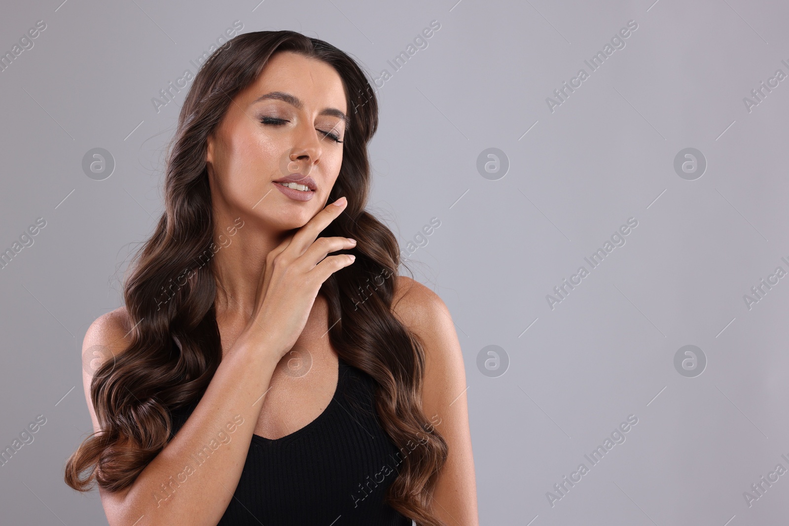 Photo of Hair styling. Beautiful woman with wavy long hair on grey background