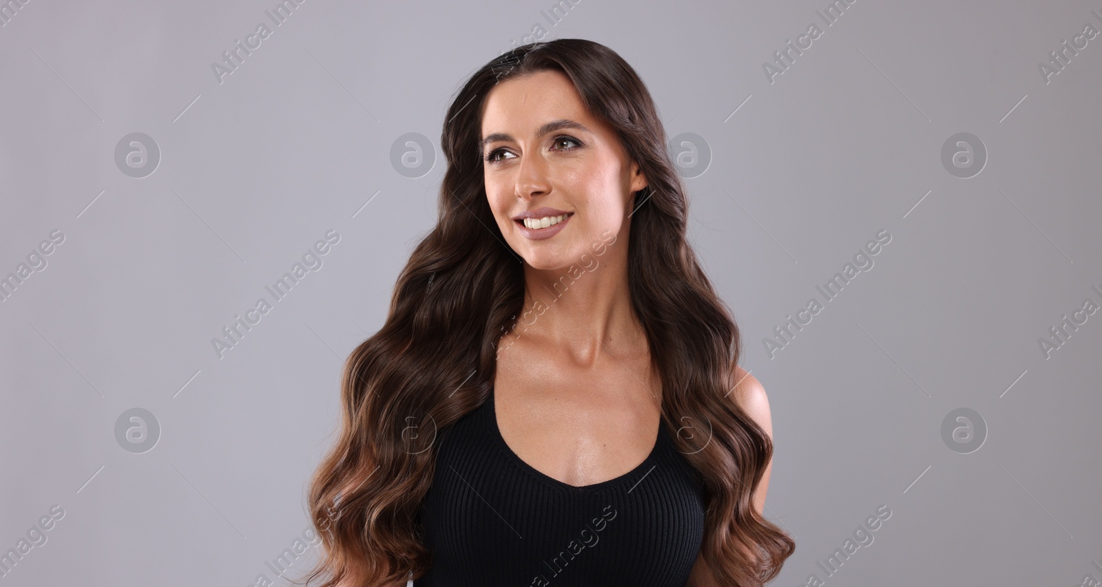 Photo of Hair styling. Beautiful woman with wavy long hair on grey background