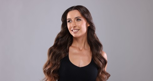 Photo of Hair styling. Beautiful woman with wavy long hair on grey background